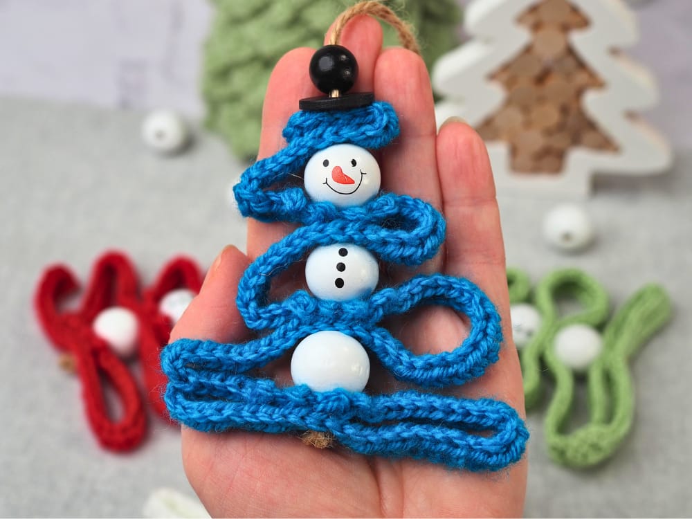 Close-up of a blue crochet snowman ornament, showing the snowman head bead and top hat.