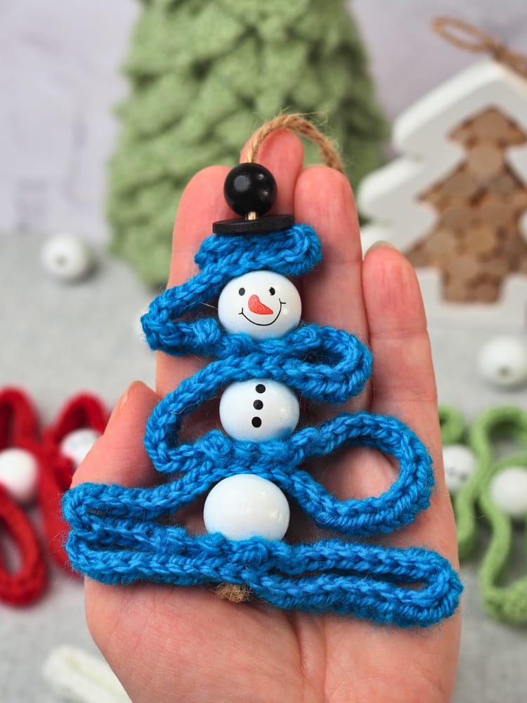 Close-up of a blue crochet snowman ornament, showing the snowman head bead and top hat.